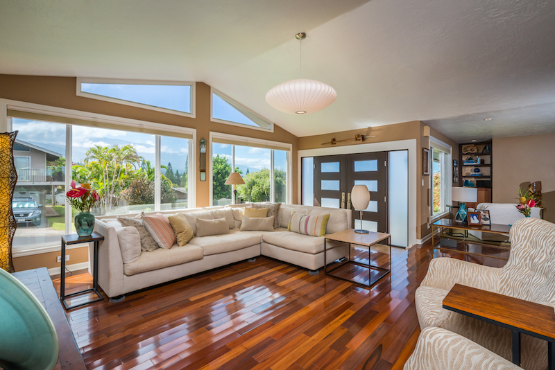 Big Windows that let in lots of light, tiger wood floors, vaulted ceilings and a pendant light highlight the living room of this Pukalani Home